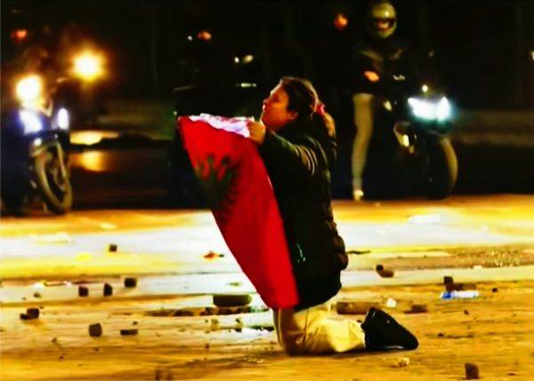 Albaneză, la protestele din Tirana, îngenunchiată în faţa poliţiştilor, oferindu-le drapelul ţării; în momentele următoare, un poliţist a ridicat-o, a sărutat drapelul şi a îmbrăţişat-o. Albaneză, la protestele din Tirana, îngenunchiată în faţa poliţiştilor, oferindu-le drapelul ţării; în momentele următoare, un poliţist a ridicat-o, a sărutat drapelul şi a îmbrăţişat-o.